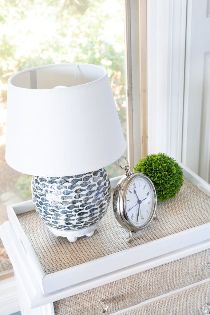 looking down on a night table with a fish pattern lamp, clock and green plant.