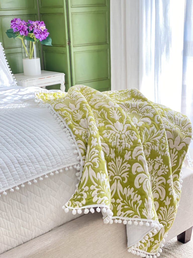 green and white throw blanket laying over the end of a bed with white bedding.