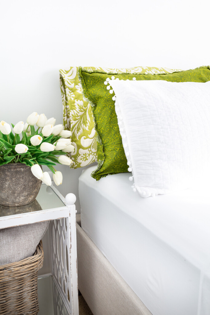 3 green and white pillows on a bed with white tulips on a bedside table