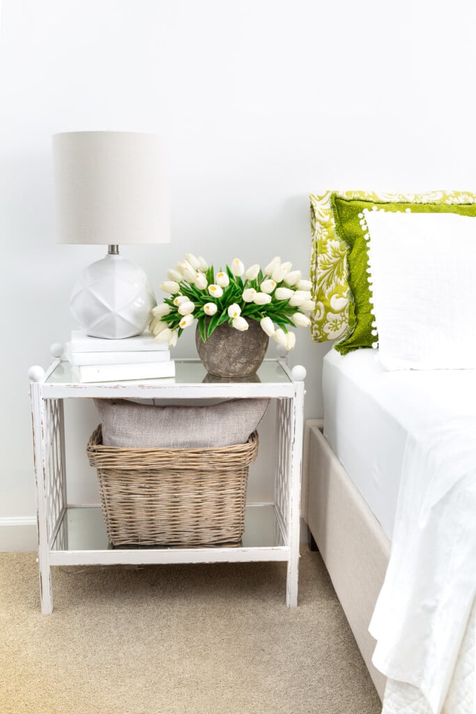 White and green guest room - bed and night table with lamp and vase of tulips