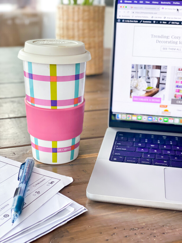 colorful travel coffee mug on table with computer next to it.