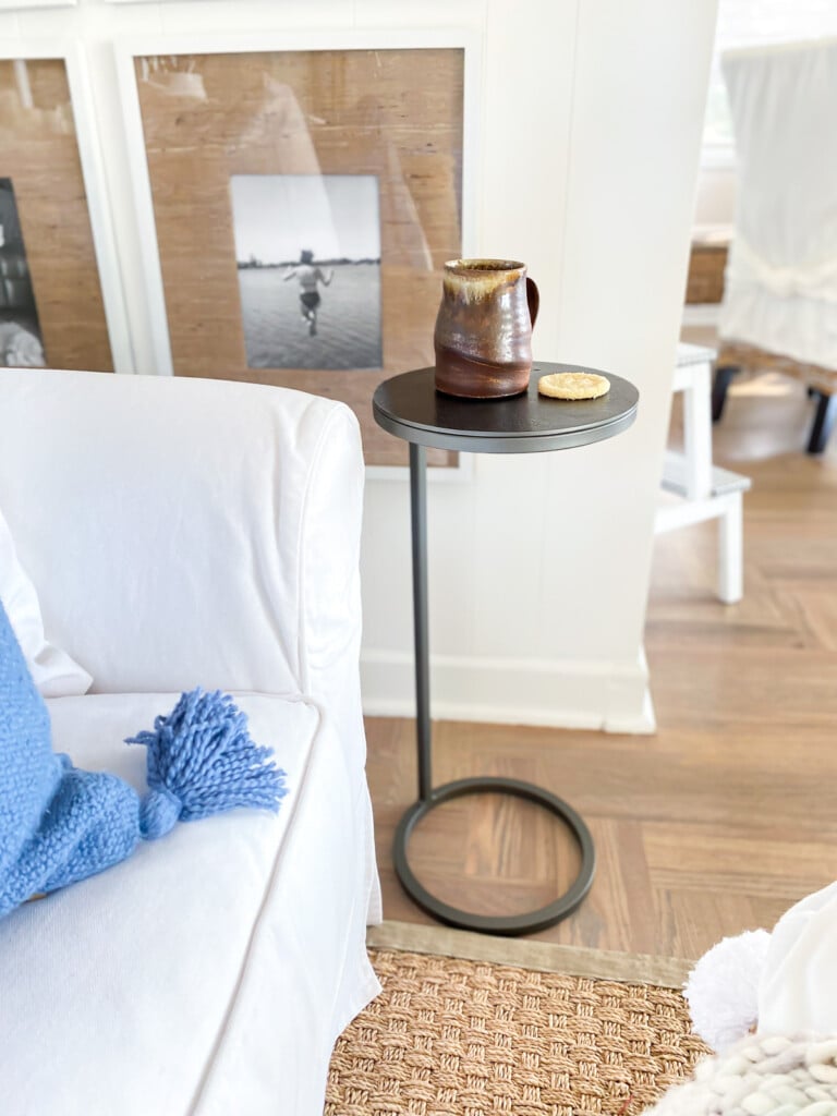 A Duke Round Accent table next to. white sofa with a light blue pillow on it.