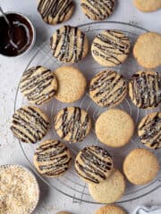 Vegan coconut cookies on a wire cooling rack with bowls of melted chocolate and toasted coconut.