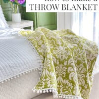 Green and white pom-pom trimmed throw draped over the end of a bed. Text overlay says - how to make a throw blanket
