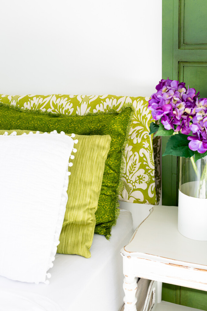 green and white bedding on a bed with a vase of purple hydrangeas on a night table.