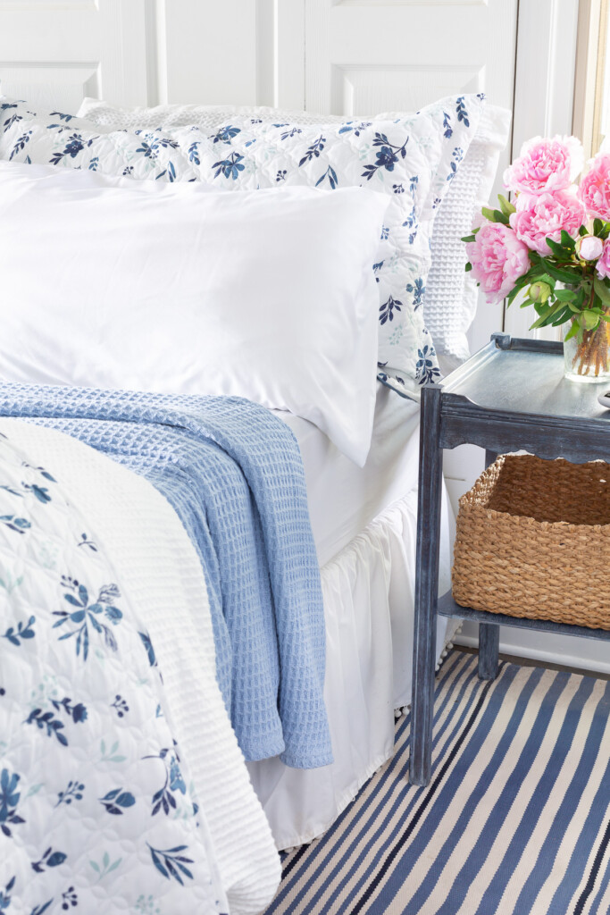 A king size bed made up in a reversible floral bedspread, waffle weave duvet cover and sky blue blanket.