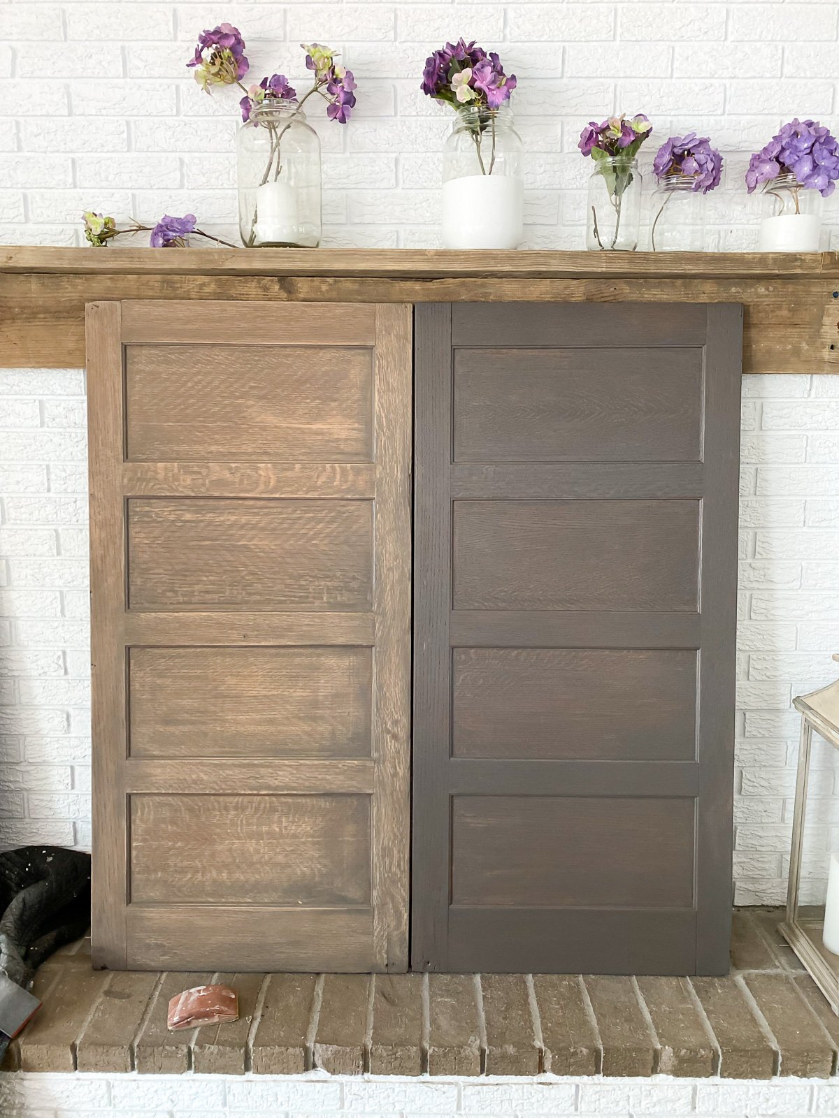 two wood panels leaning against a fireplace wall. One is sanded to lighten in, the other is stained in a driftwood shade.