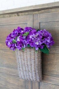 hanging basket filled with purple hydrangeas on the wood panels that were made into a way to cover a fireplace.