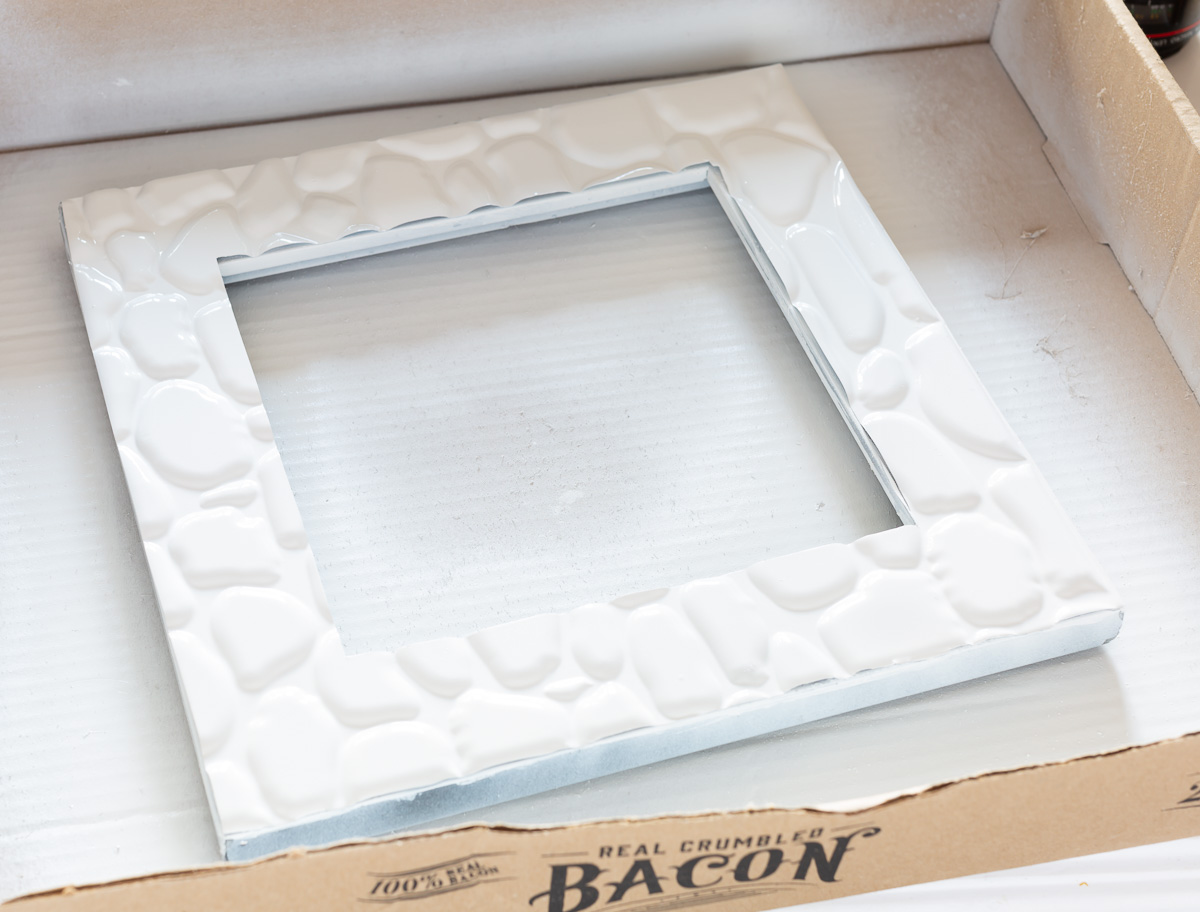 spray painted faux adhesive tile in a spray painting box.