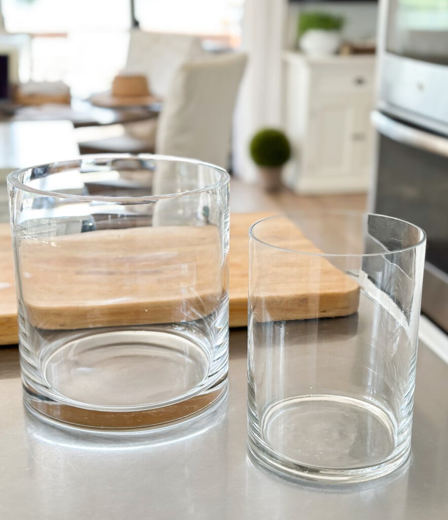 two plain glass vases on a counter to be placed one inside the other to make candle vase.