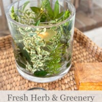 Fresh herb and greenery DIY candle vase on a wicker tray table in a living room.