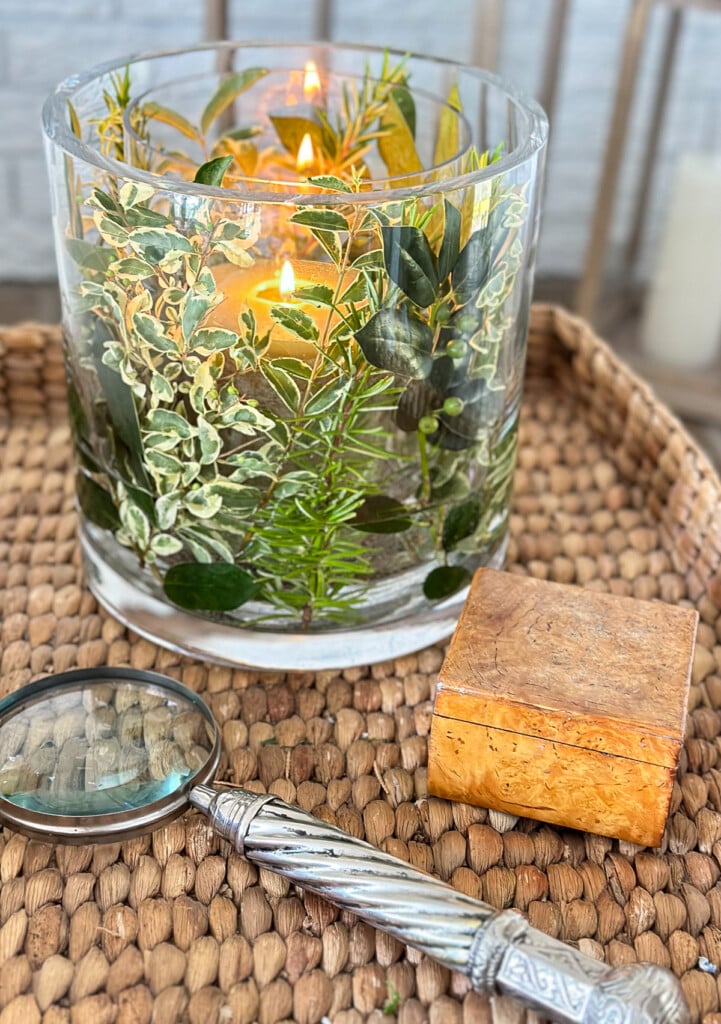 Close up of fresh herb and greenery DIY candle vase on a wicker tray table in a living room.