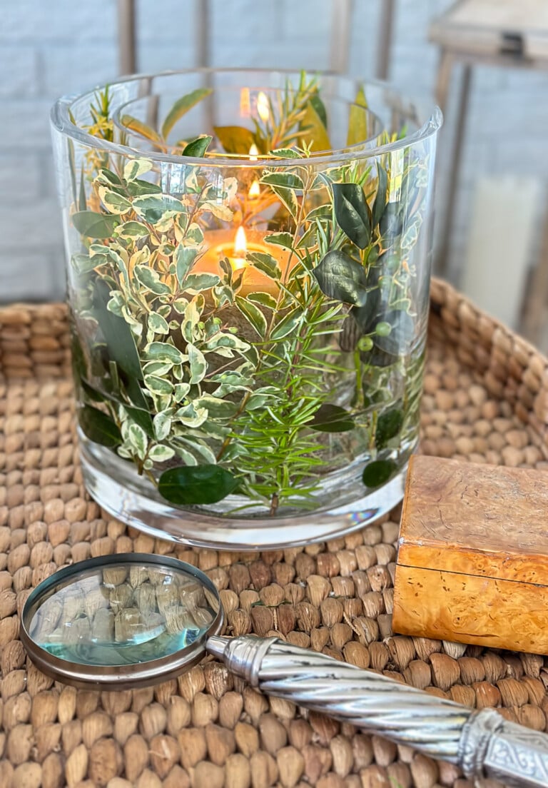 Fresh herb and greenery DIY candle vase on a wicker tray table in a living room.