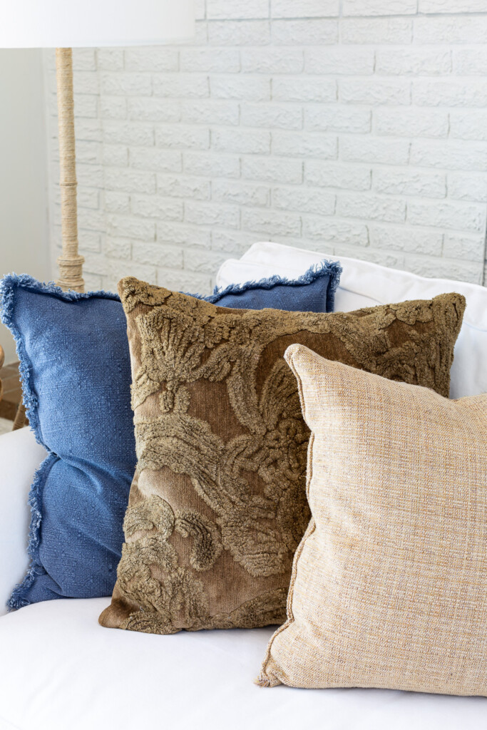 3 pillows lined up on a white sofa. One is summer blue and the other two brown and beige to slowly add warmer colors to the room.