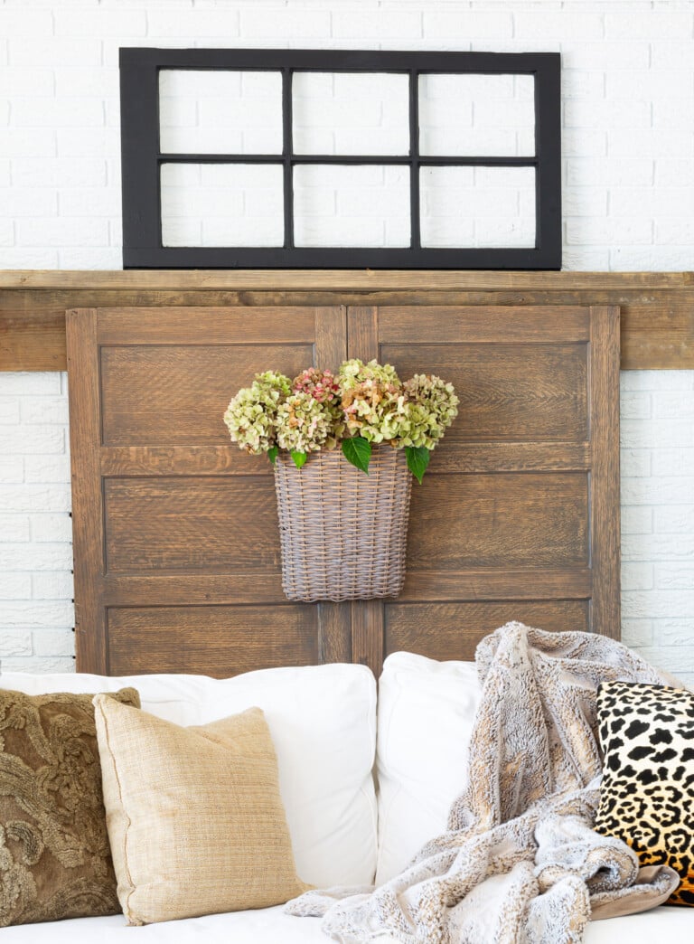 Wood door covered fireplace with a black window sash on mantel, white sofa and pillows in fall colors.