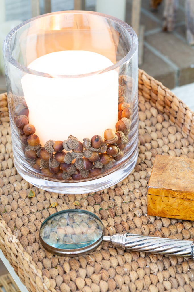 faux acorns in glass candle vase on table decorated for fall.