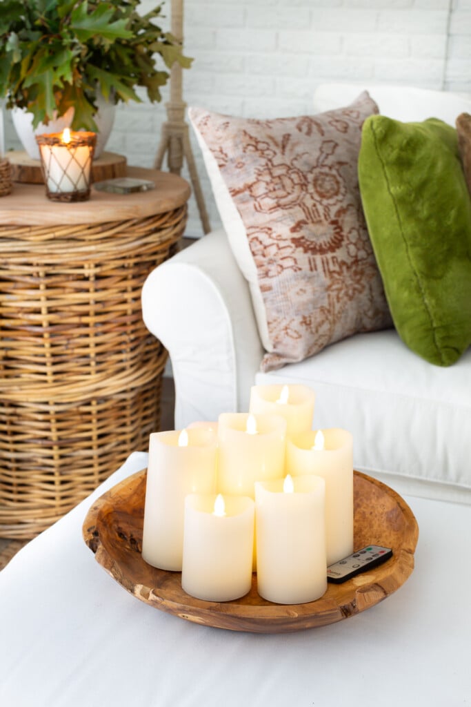 Large wood bowl on ottoman filled with battery operated off-white pillar candles in a living room.