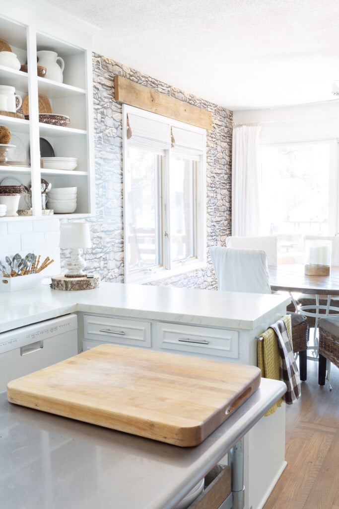 Peel and stick stacked stone wallpaper on a accent wall in a white kitchen.