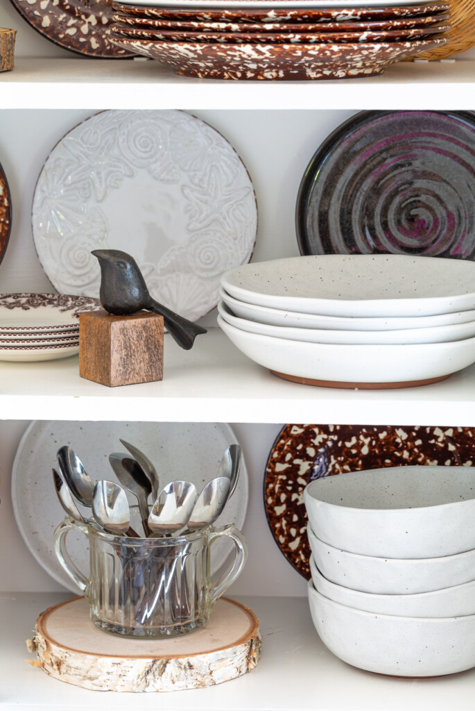 A collection of plates displayed on open shelves in a kitchen, mixed in with a few decorative fall accessories.