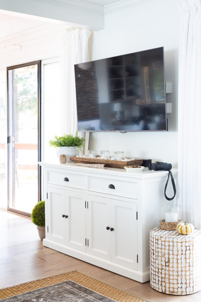 Black flat screen TV mounted on wall with white sideboard underneath.