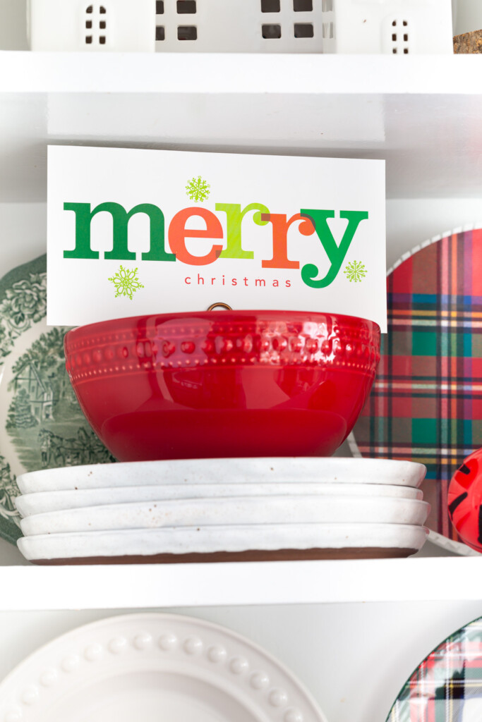 Christmas card in red bowl on open shelf that says merry.