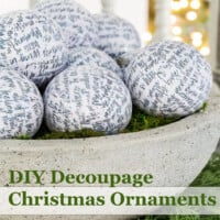 DIY Decoupage Christmas Ornaments in a stone bowl placed on pine greenery.