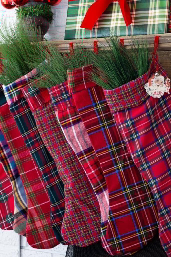 red plaid handmade stockings hanging from a wood mantel.