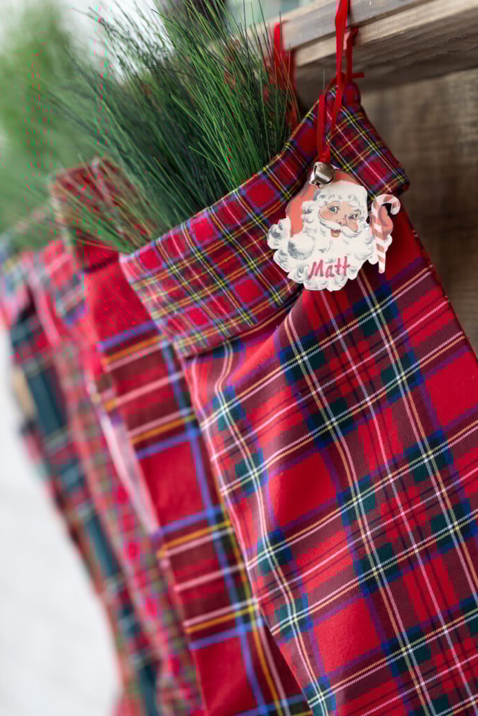 A line up of red plaid Christmas stockings hanging on a wood mantel.