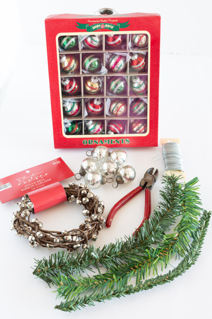 materials needed to make Christmas candle rings DIY. Mini Shiny Brite ornaments, garland ties, jingle bells and a wire cutter.