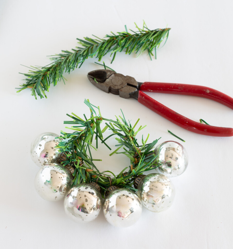 How to thread small Christmas ornaments on on a garland tie to make a candle ring.