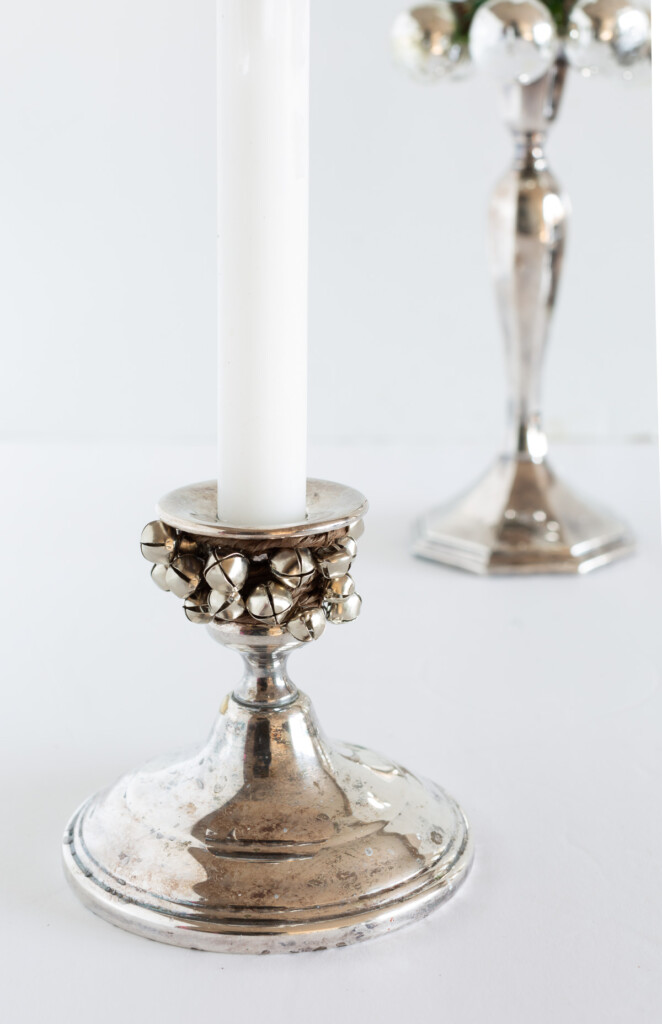 Silver candlestick holder with a garland of mini jingle bells tied around the neck.