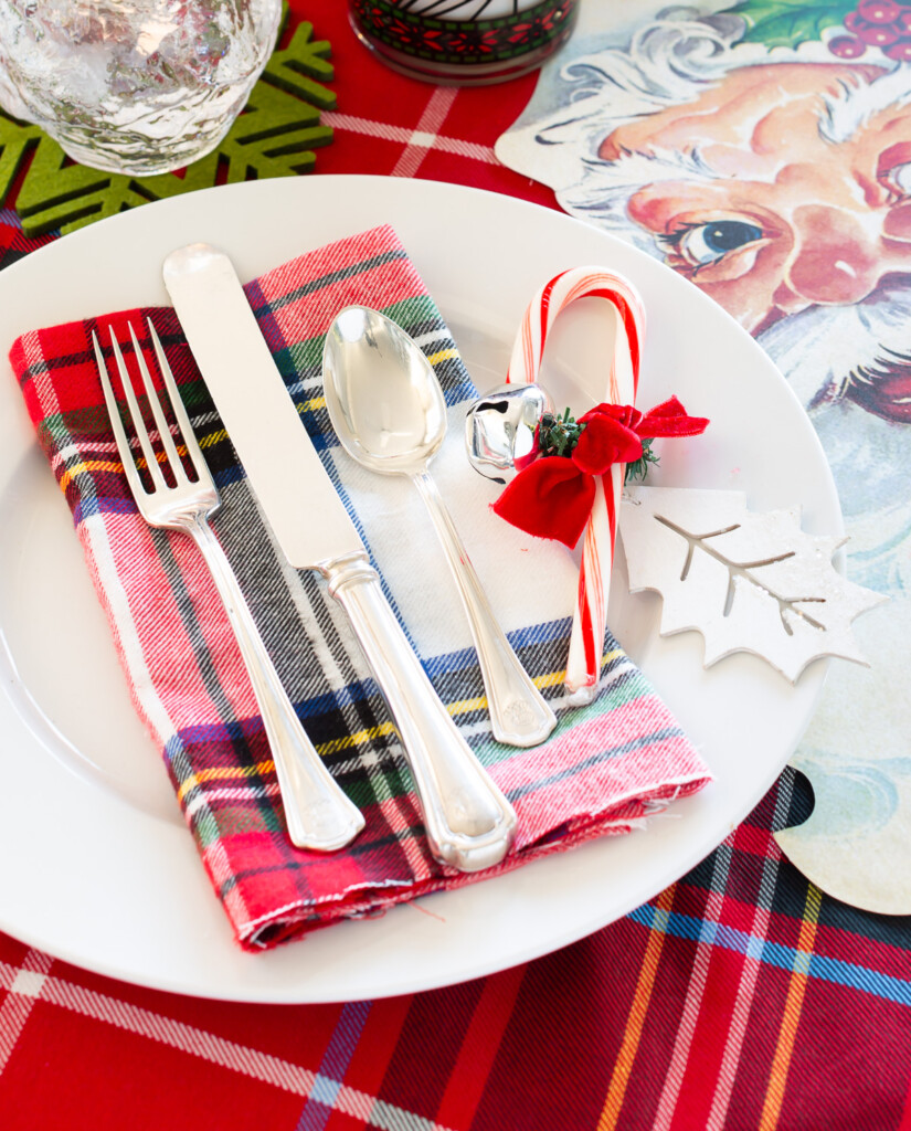 Christmas table setting ideas red and white with plaid and Santa accents. Candy cane and jingle bell on plate for decoration.
