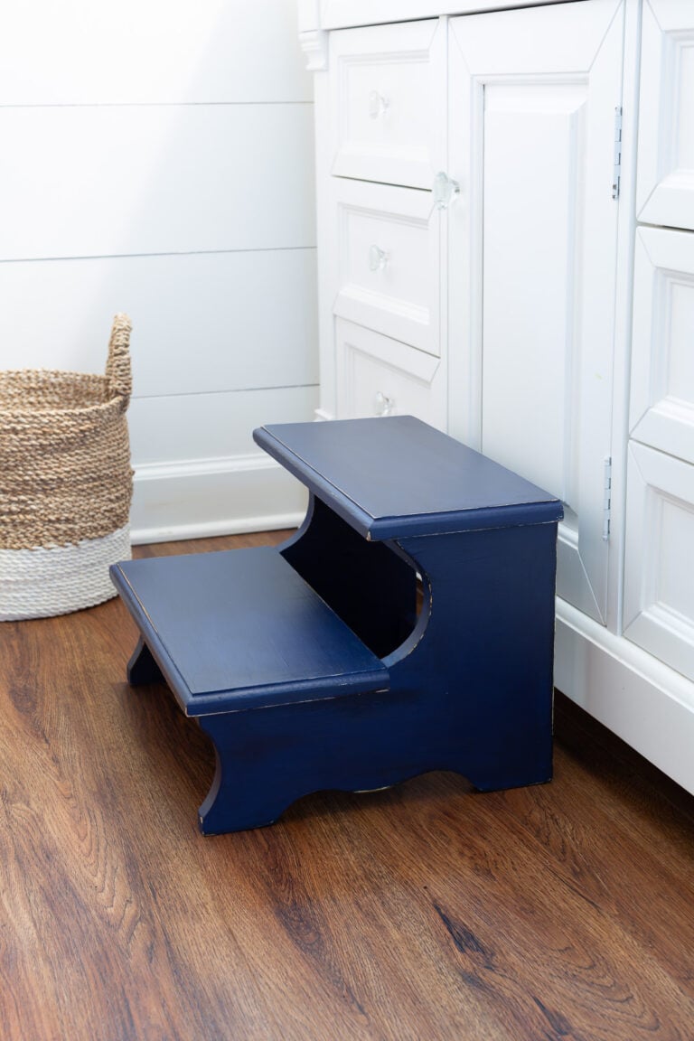 After photo of a Thrift store wood step stool painted with Navy blue chalk paint. Placed in front of a white bathroom vanity.
