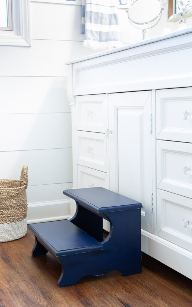 After photo of a Thrift store wood step stool painted with Navy blue chalk paint. Placed in front of a white bathroom vanity.