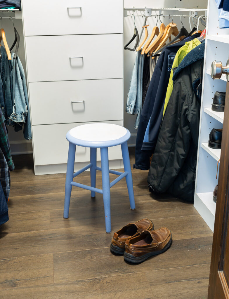 19" high round wood stool painted light blue and white in a clothes closet to sit on so you can put on shoes.