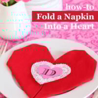 Red cloth napkin folded into a heart shape on white dinner plate to celebrate Valentine's Day.