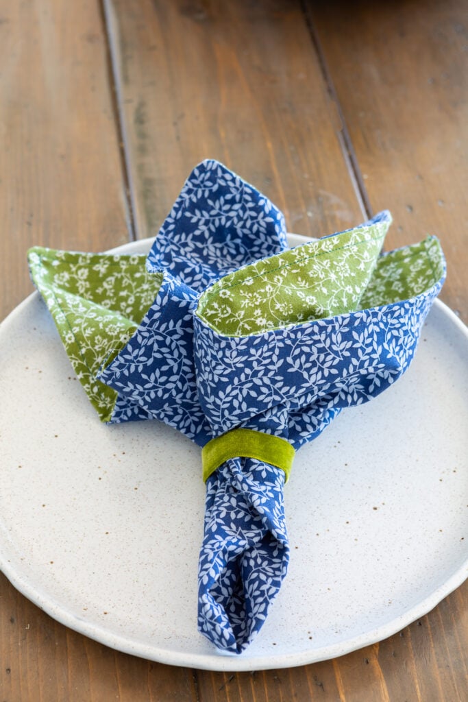 2 sided cloth napkin gathered together with a plain napkin ring on a dinner plate.
