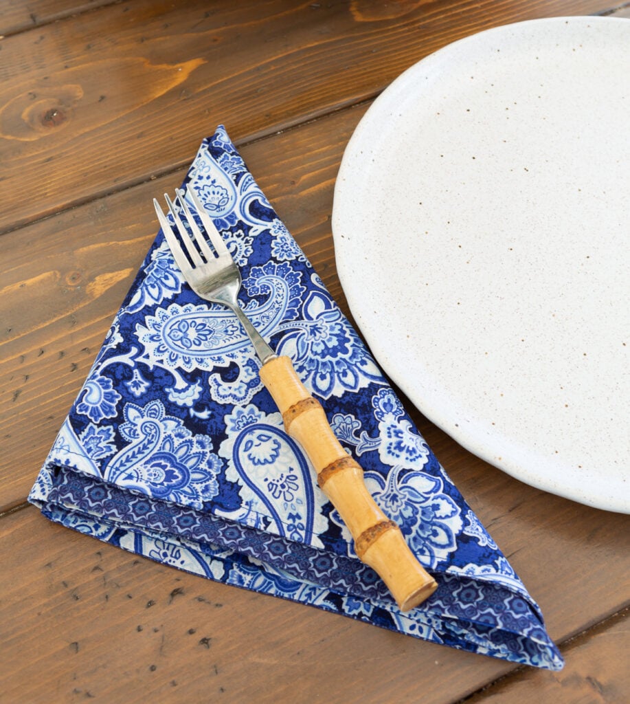 Blue and white cloth napkin folded in a triangle shape next to a dinner plate.