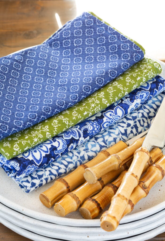 4 blue, white and green patterned napkins folded on a plate with bamboo utensils.