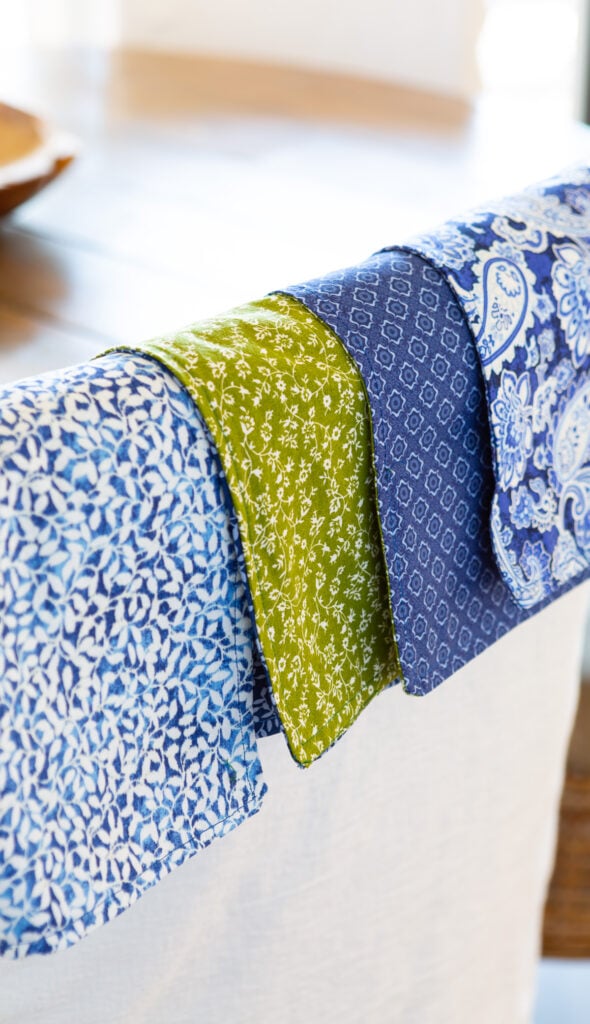 4 two-ply cloth napkins hanging over the back of a dining chair.