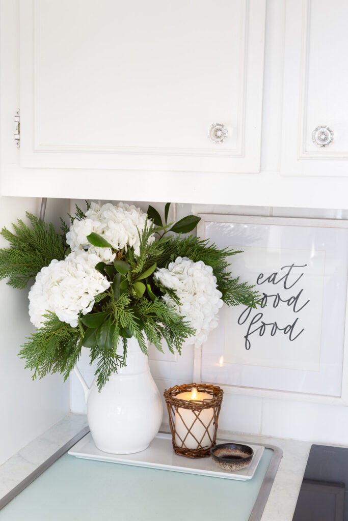 Winter white large head hydrangeas and greenery mixed in a white pitcher becomes cheery winter decor.