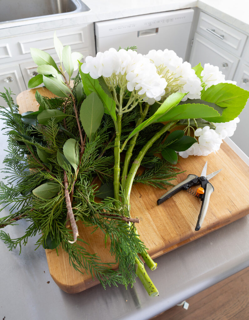 Faux white hydrangeas and evergreen clippings from my yard placed on worktable.