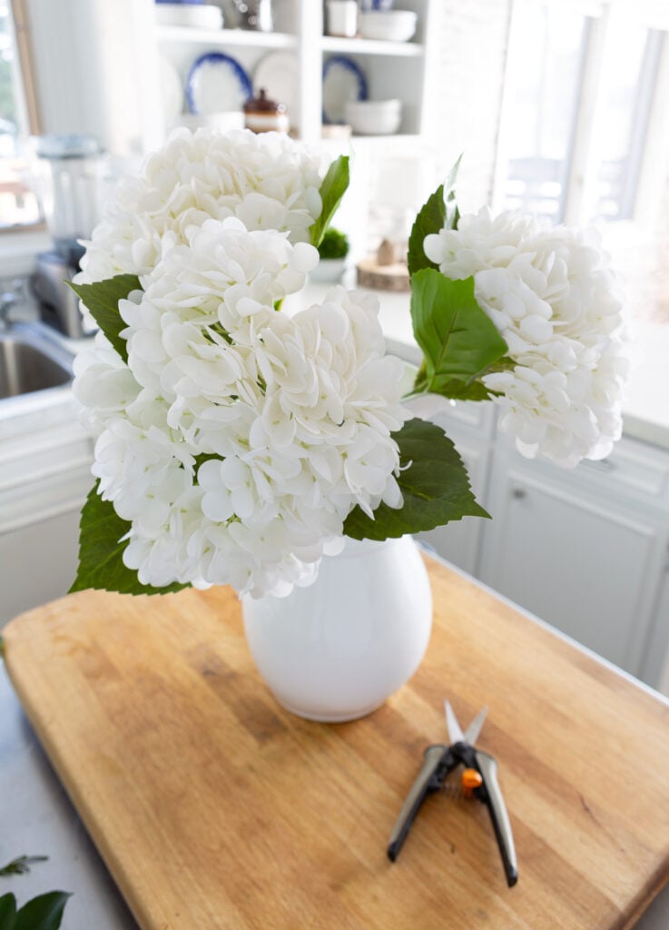 3 faux winter white hydrangeas in a white pitcher on a kitchen counter.