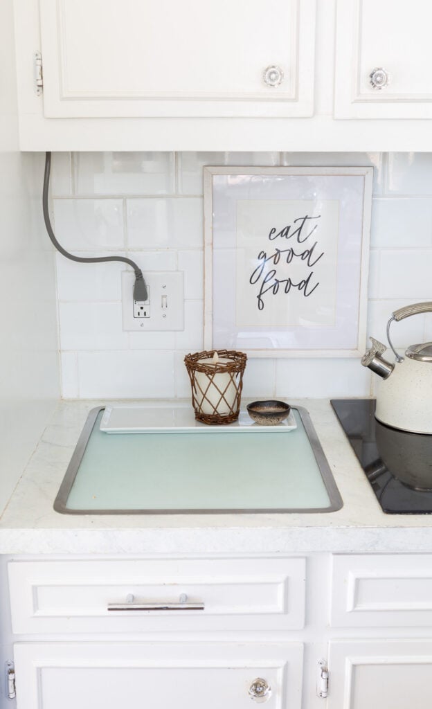 A corner on a kitchen counter and backsplash where an electrical cords comes down from the upper cabinets.