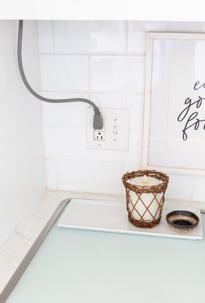 A corner on a kitchen counter and backsplash where an electrical cords comes down from the upper cabinets.