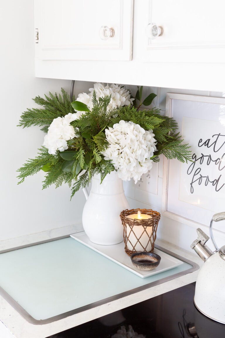 Winter white large head hydrangeas and greenery mixed in a white pitcher becomes cheery winter decor.