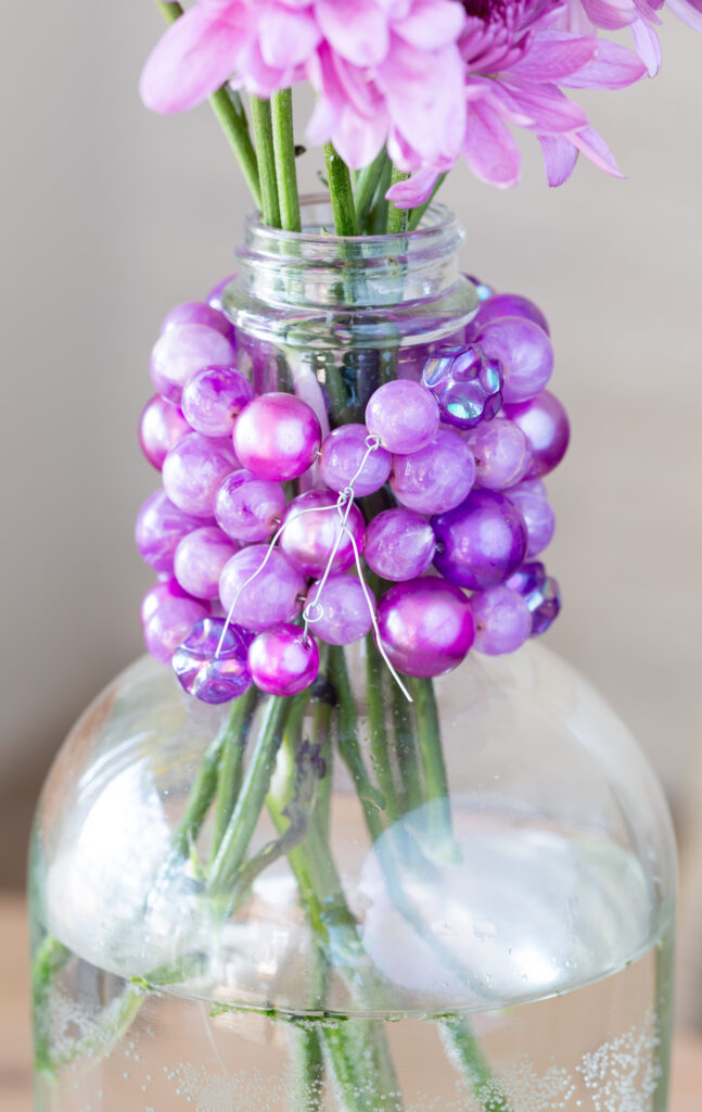 How to use florist wire to attach a old costume jewelry necklace around a glass bottle to make a pretty vase.