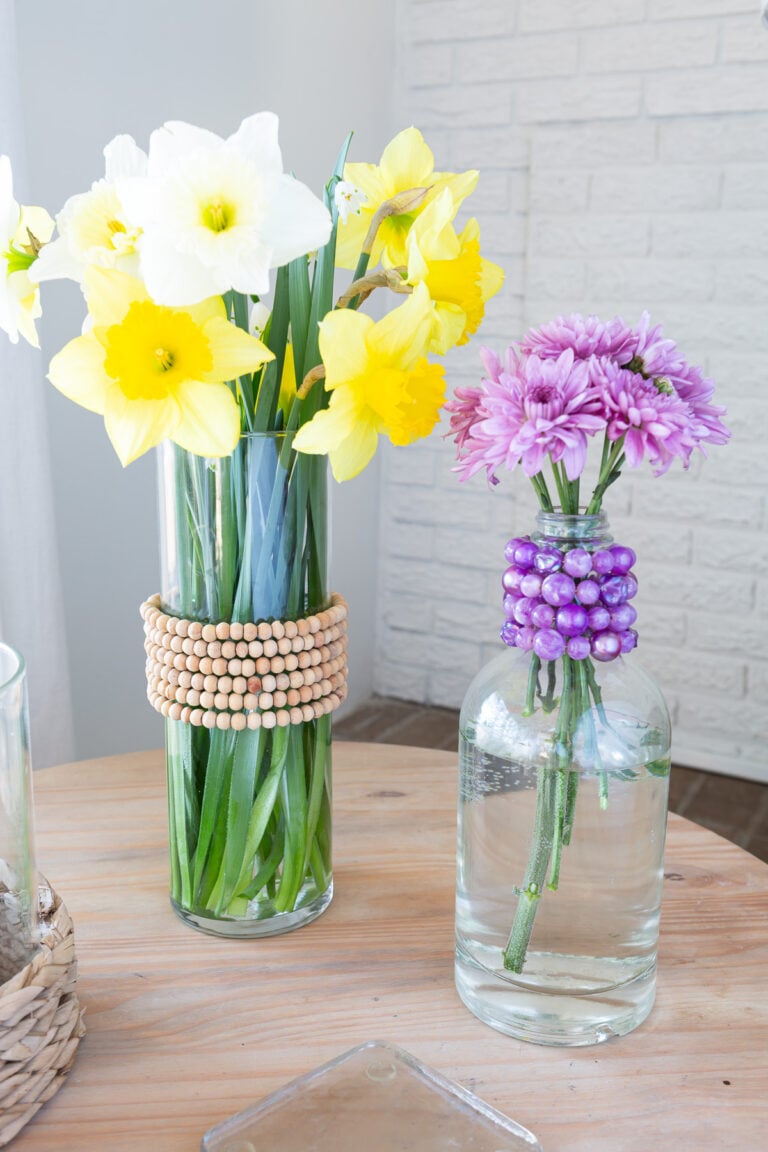1 glass vase and 1 glass bottle with old jewelry necklaces wrapped around them to create colorful spring decor.