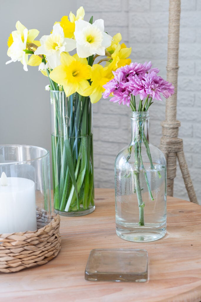 1 glass vase and bottle with spring flowers in them.