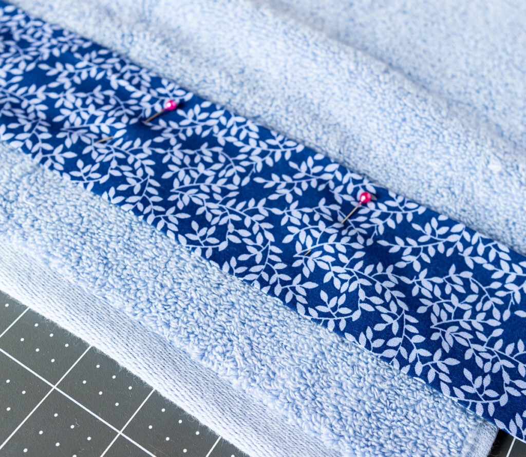 blue fabric being pinned to a bath towel before sewing it on.